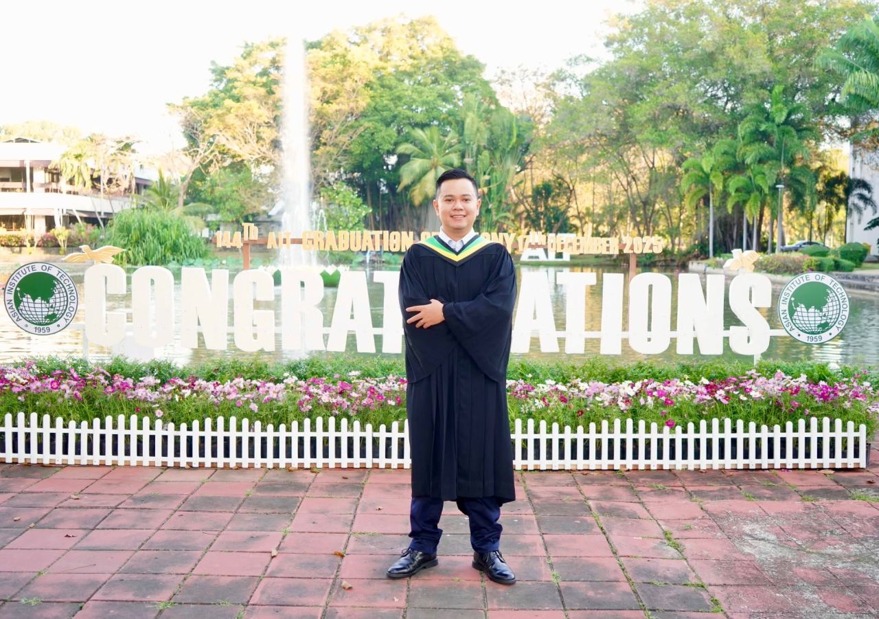 Khoa at his Asian Institute of Technology graduation, wearing an academic gown in front of the congratulations display.